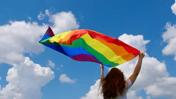 Gökyüzü arka planında LGBT bayrağı tutan kişi — Stok fotoğraf