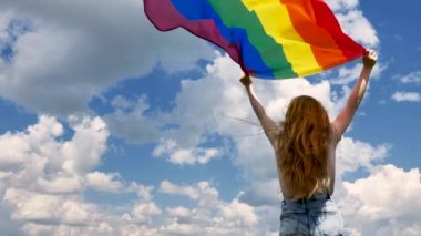 Gökyüzü arka planında LGBT bayrağı tutan kişi