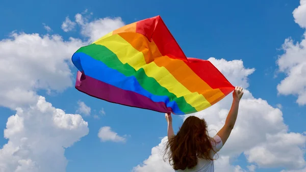 Gökyüzü arka planında LGBT bayrağı tutan kişi — Stok fotoğraf