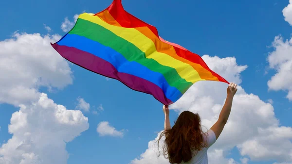 Gökyüzü arka planında LGBT bayrağı tutan kişi