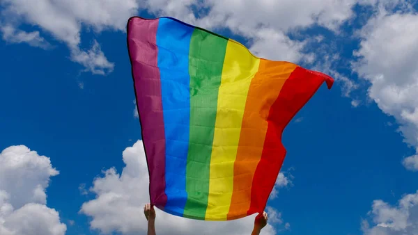 Gökyüzü arka planında LGBT bayrağı tutan kişi — Stok fotoğraf