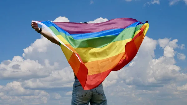 Gökyüzü arka planında LGBT bayrağı tutan kişi