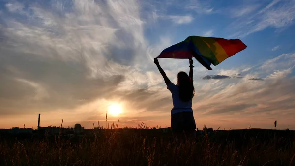 Günbatımı arkaplanında LGBT bayrağı olan kadın