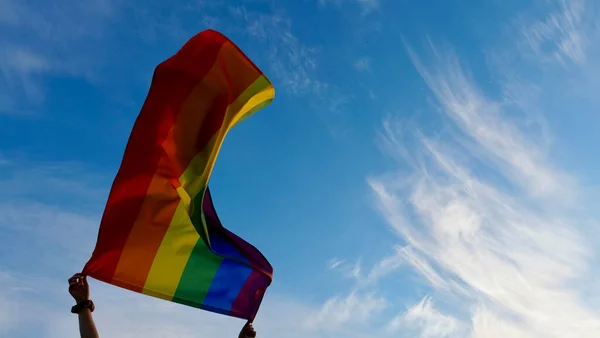 在天空背景下高举LGBT旗的人 — 图库照片