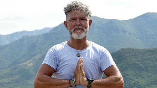 Portrait a senior man with gray hair and beard practicing meditation with prayer hands pose outdoors. spiritual practice, and mindfulness in nature