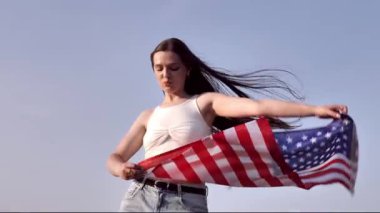Genç bir kadın açık mavi gökyüzüne karşı büyük bir Amerikan bayrağı sallıyor. Saçları rüzgarda savruluyor, Amerika 'da özgürlüğü, vatanseverliği ve gururu simgeliyor..