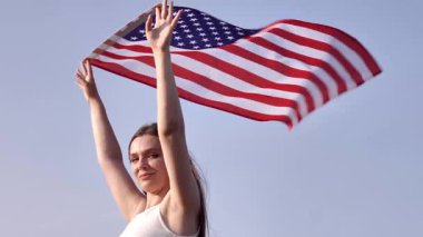 Genç bir kadın açık mavi gökyüzüne karşı büyük bir Amerikan bayrağı sallıyor. Saçları rüzgarda savruluyor, Amerika 'da özgürlüğü, vatanseverliği ve gururu simgeliyor..