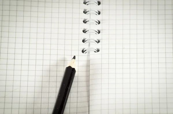 Black pencil on a background of the disclosed notepad. — Stock Photo, Image
