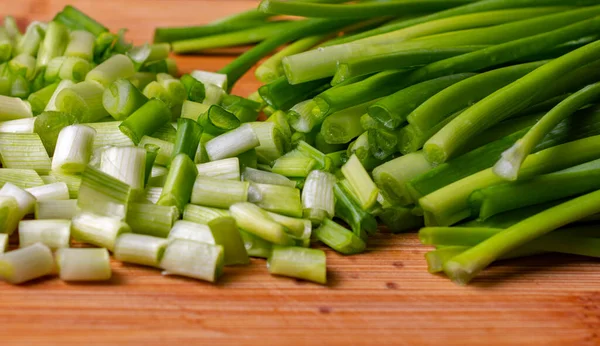 Close up of chopped green spring onions on wooden board.