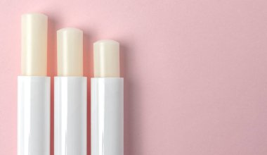 Pembe arka planda üç dudak kremi tüpünün üst görüntüsü.