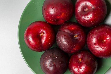 Yeşil tabakta büyük kırmızı eriklerin üst görüntüsü.