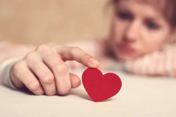 Sad girl is holding heart symbol by her finger