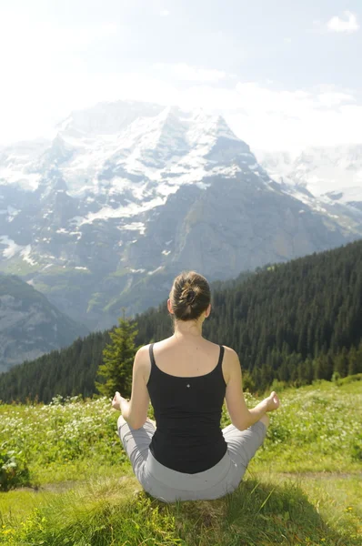 Girl in a meditation pose on a green meadow in mountains — Stock Photo, Image
