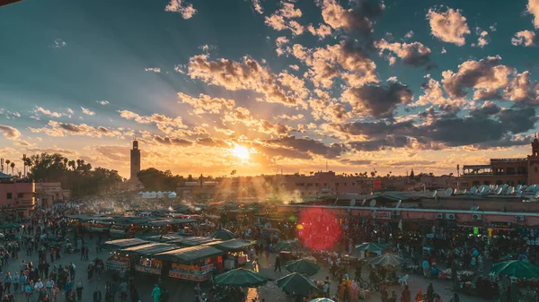 市場や人々の群衆と日没の背景にモスクの塔とヤマエルフナ広場 旅行のコンセプト モロッコのマラケシュ — ストック写真