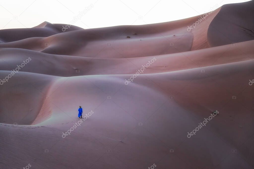 Unrecognizable Berber man walking on a dreamy desert at Twilight of dawn. Desert dune of Erg Chigaga, at the gates of the Sahara. Morocco. Concept of travel and adventure.