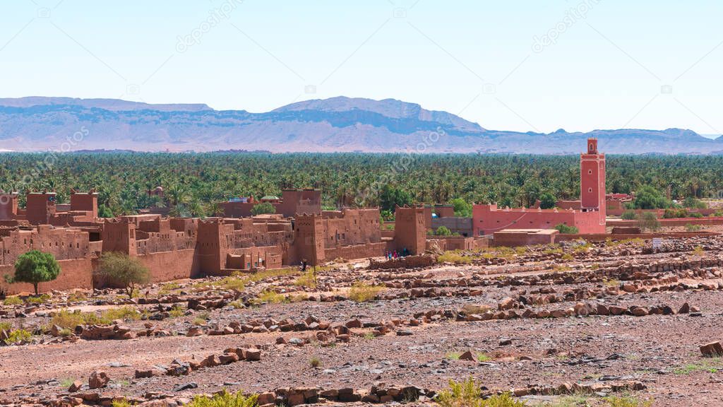 Adobe buildings in the foreground and palm forest and mountains of the Draa Valley, Zagora, Morocco.