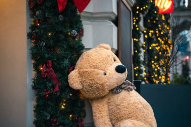 Papyonlu büyük oyuncak ayı Noel süslerinin yanında oturur. Işıklar ve çelenkler sokağı şenlikli gösteriyor. Yüksek kalite fotoğraf