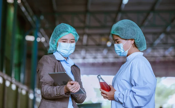 Worker of science in bottle beverage factory wearing safety  hat and face mask working to check quality of drink Basil seed produce on conveyer belt before distribution to market business