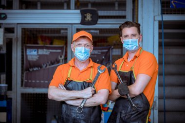Otomobil tamircileri garajda tornavida göstererek poz veriyorlar. Virüsü ve kirliliği korumak için maske takıyoruz..