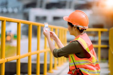 Atık su arıtma göleti endüstrisinin kontrolü altında güvenlik üniforması giyen işçiler, su destek endüstrisini kontrol etmek için büyük çaplı başka bir işçiyle iletişim kurmak için radyo iletişimini kullandı..