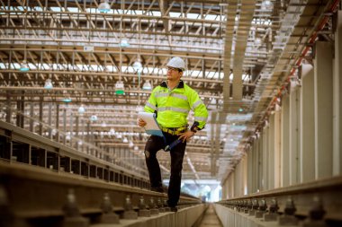 Portre mühendisi teftiş altında ve inşaat sürecini kontrol ediyor ve tren istasyonunda çalışmalarını kontrol ediyor. İş yerinde güvenlik üniforması ve güvenlik kaskı takan mühendis.
