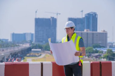 Portre mühendisi teftiş altında ve inşaat sürecini kontrol ediyor ve tren istasyonunda çalışmalarını kontrol ediyor. İş yerinde güvenlik üniforması ve güvenlik kaskı takan mühendis.