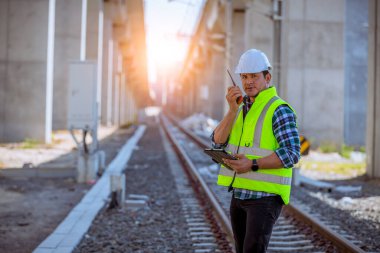 Portre mühendisi teftiş altında ve inşaat sürecini kontrol ediyor ve tren istasyonunda çalışmalarını kontrol ediyor. İş yerinde güvenlik üniforması ve güvenlik kaskı takan mühendis.