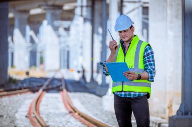 Portre mühendisi teftiş altında ve inşaat sürecini kontrol ediyor ve tren istasyonunda çalışmalarını kontrol ediyor. İş yerinde güvenlik üniforması ve güvenlik kaskı takan mühendis.