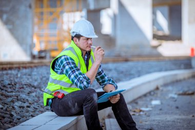 Portre mühendisi teftiş altında ve inşaat sürecini kontrol ediyor ve tren istasyonunda çalışmalarını kontrol ediyor. İş yerinde güvenlik üniforması ve güvenlik kaskı takan mühendis.