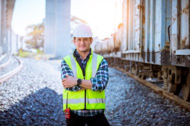 Portre mühendisi teftiş altında ve inşaat sürecini kontrol ediyor ve tren istasyonunda çalışmalarını kontrol ediyor. İş yerinde güvenlik üniforması ve güvenlik kaskı takan mühendis.