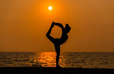 Siluet spor kadını sabah kumsalda yoga egzersizi yapıyor. Yoga meditasyon sağlık sporu konsepti..