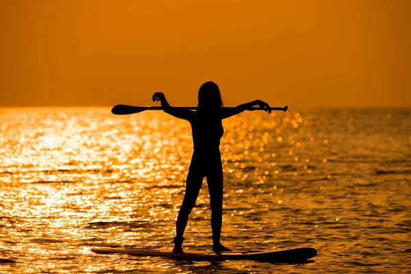 Silhouette sport girl stand up paddling on sup board or surfboard enjoy to play extreme sport on holidays at sunlight beach.