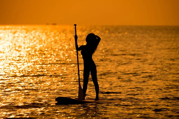 Silhouette sport girl stand up paddling on sup board or surfboard enjoy to play extreme sport on holidays at sunlight beach.