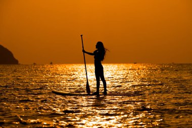 Siluet sporcusu kız yemek masasında ya da sörf tahtasında kürek çekerek güneşli plajlarda ekstrem sporlar yapmayı sever..