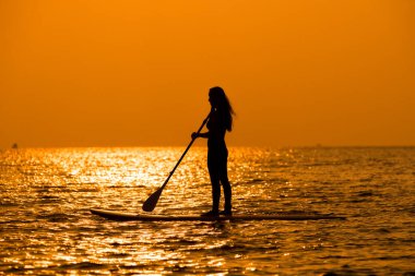 Siluet sporcusu kız yemek masasında ya da sörf tahtasında kürek çekerek güneşli plajlarda ekstrem sporlar yapmayı sever..