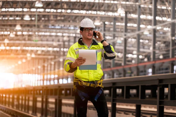 Engineer railway under inspection and checking construction process train work shop and railroad station .Engineer wearing safety uniform and helmet by holding document in work.