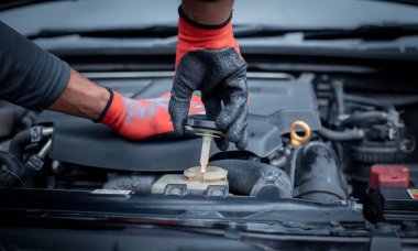 Araba tamircisi açık araba kaputu tamiratı araba garajında yeni benzin doldurmak ve bakım için motor seviyesini kontrol ediyor..