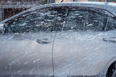 Araba yıkamacıda çalışan bir işçi, müşteri arabasını sabunla temizlemeye çalışıyor, araba servisi kavramı..