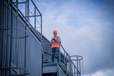 Endüstri soğutma kulesi klimasını kontrol altında tutan mühendis, hava kirliliğini korumak için maske takan, büyük endüstriyel binanın soğutma kulesi soğutma soğutma soğutma soğutma soğutma soğutma soğutma havalandırması havalandırması..