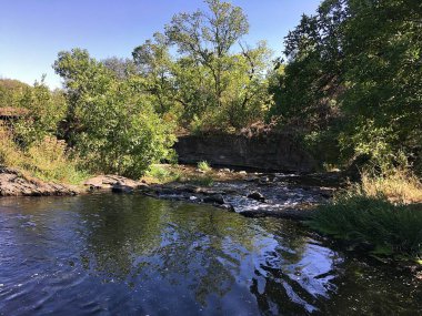 İskelenin yanındaki hızlı nehir. Suyun üzerindeki büyük ağaçlar. Suda yansıma. Şehrin dışında dinlen..