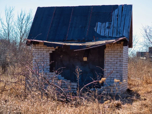Gebroken stenen huis met een gebroken dak op een zonnige lentedag tussen de gele struiken van gras. — Stockfoto