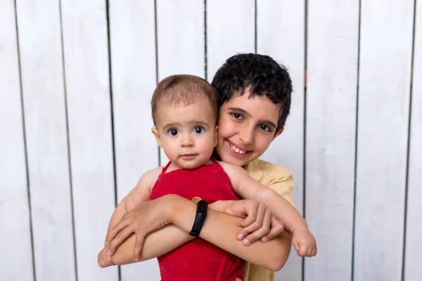 Happy brother holding a newborn baby boy in his arms on the white background. Brothers, family, friends. Newborn photosession.