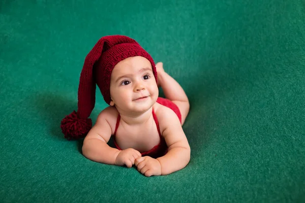 Cute newborn baby in the red hat. Happy baby on a green background. Closeup portrait of newborn baby. Baby goods packing template. Nursery. Medical and healthy concept. Christmas. New Year