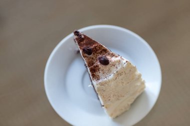 Beyaz bir porselen tabakta servis edilen tek bir dilim Kara Orman kapağının (Schwarzwalder Kirschtorte) yüksek açılı yakın çekim görüntüsü. Tarafsız bir arkaplanda minimalist kompozisyon, yemek blogları, menüler veya fırın reklamları için mükemmel