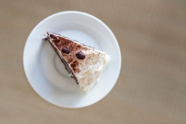 Beyaz bir porselen tabakta servis edilen tek bir dilim Kara Orman kapağının (Schwarzwalder Kirschtorte) yüksek açılı yakın çekim görüntüsü. Tarafsız bir arkaplanda minimalist kompozisyon, yemek blogları, menüler veya fırın reklamları için mükemmel