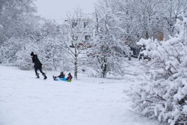 PRAG - Ocak 2021. Karlı kış manzarası. Bir kadın, çocuklu bir kızak çekiyor. Çocuklar kar kaymasından kayıyor. Karda ağaçlar. Kar yağışıweather condition. 