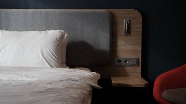 Yatak odasının boş komodini, okuma lambasını ve modern iç dizayn evi ya da otelde USB soketini içeren yakın plan bir parçası. Yumuşak yastık ve battaniye, şık rahat mobilyalar. Güneş gölgeleri.