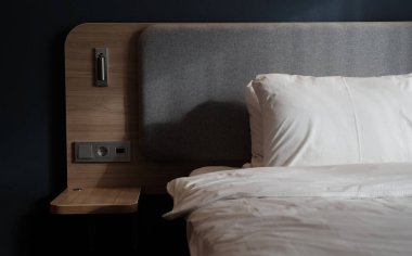 Yatak odasının boş komodini, okuma lambasını ve modern iç dizayn evi ya da otelde USB soketini içeren yakın plan bir parçası. Yumuşak yastık ve battaniye, şık rahat mobilyalar. Güneş gölgeleri.