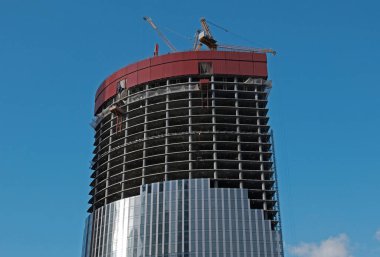 Bir gökdelen ya da konut inşaatı. Mavi gökyüzü arka planındaki inşaat alanındaki vinç ve bina yapıları. Cam aynalı ofis binasının ön dokusu.. 