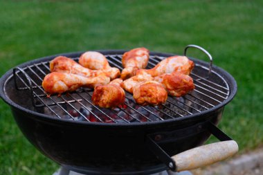 Barbekü tavuk bacağı ızgarada pişiyor. Mangal sosunda marine edilmiş tavuk budu, arka planda kırmızı kömürle kızartılmış. Kırmızı kömür ve ateşten çıkan duman. Kapat..